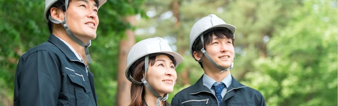 ヘルメットを着用し、笑顔で上方を見つめる3人の作業員
